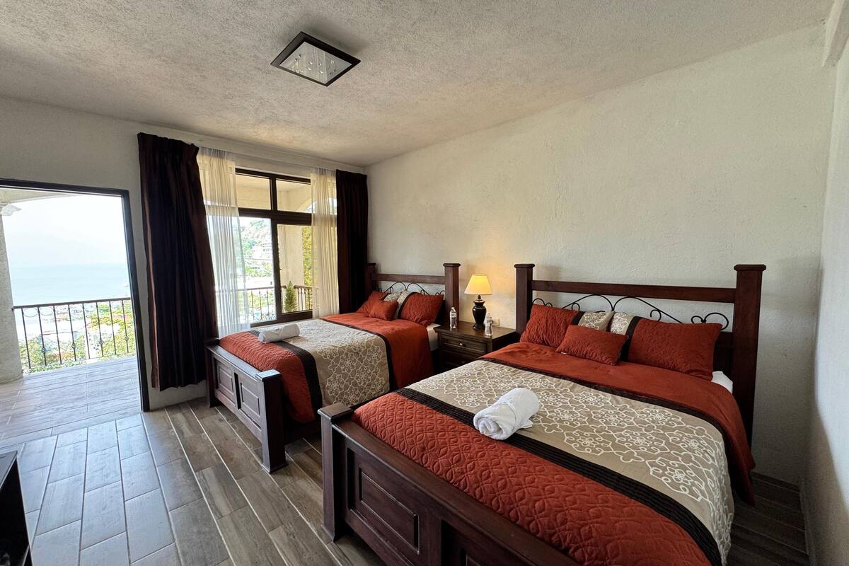 Een hotelkamer met twee bedden, een balkon met gordijnen, een klein tafeltje en een nachtkastje met een lamp.
