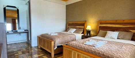 A hotel room with two wooden beds, a herringbone-patterned floor, a ceiling light, and a mirror in the corner.