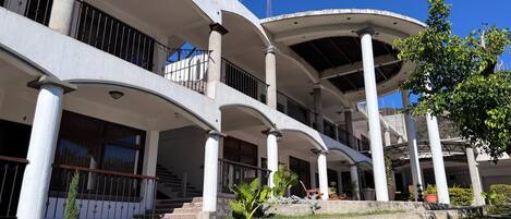 Un edificio de varios pisos con fachada curva, múltiples balcones y un jardín ajardinado.