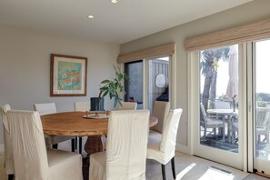 A dining area with a wooden table and white chairs, a potted plant, and a painting on the wall. - Beachfront Ocean Dream on the Sand (Hilton Head Island)