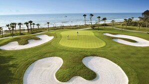 En golfbana med sandbunkrar, fri utsikt över havet och palmer.