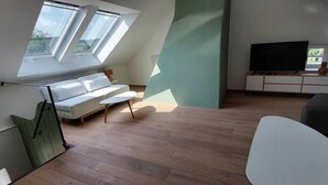 Una sala de estar moderna con un sofá blanco, un televisor de pantalla plana y un ventanal grande con tragaluces.