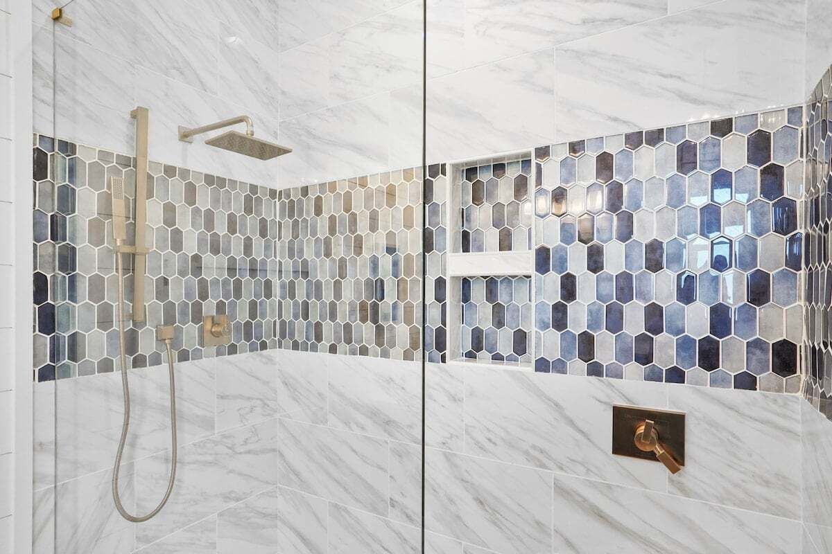 A shower with a hexagonal tile pattern and a marble floor.