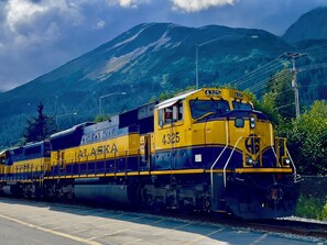 Un tren de Alaska amarillo y azul, número 4325, sobre rieles, con montañas al fondo.