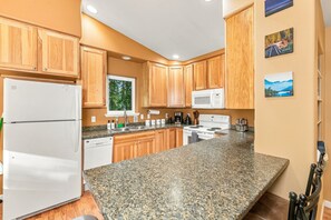 A kitchen with wooden cabinets, a granite countertop, a white refrigerator, a microwave, a stove, and a sink.