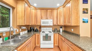A kitchen with wooden cabinets, a stainless steel sink, a white stove, and a microwave.