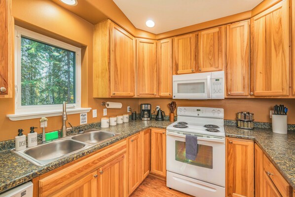 A kitchen with wooden cabinets, a white microwave, a stove, and a sink.