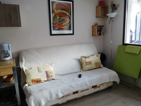 A small, cozy room with a white sofa, two patterned pillows, a remote control, a coffee maker, a lamp, and a green easel. - Large south-facing studio (Saint-Pierre-de-Chartreuse)