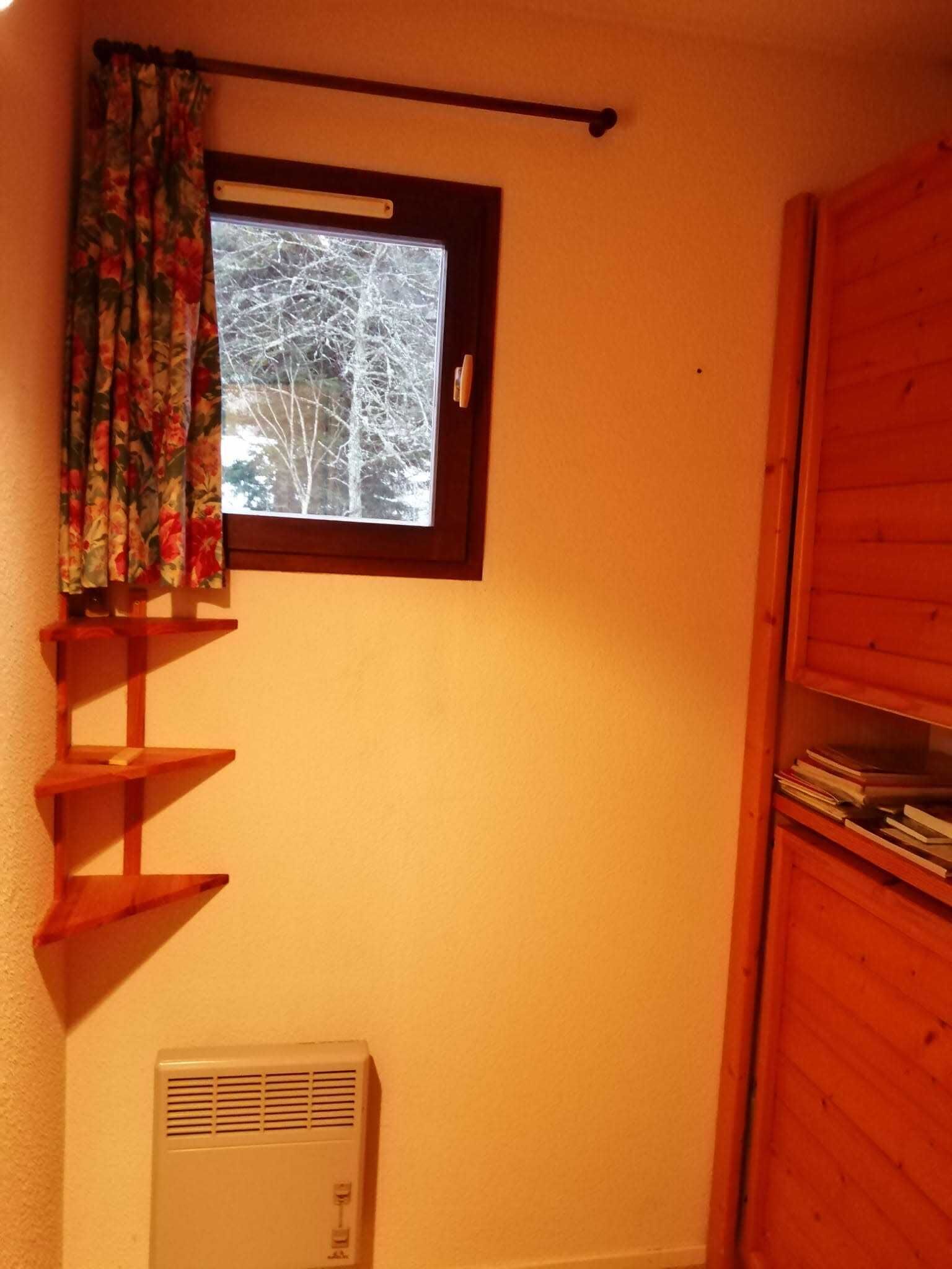 A room with a window, a wooden shelf, and a white air conditioning unit.