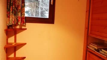 A room with a window, a wooden shelf, and a white air conditioning unit.