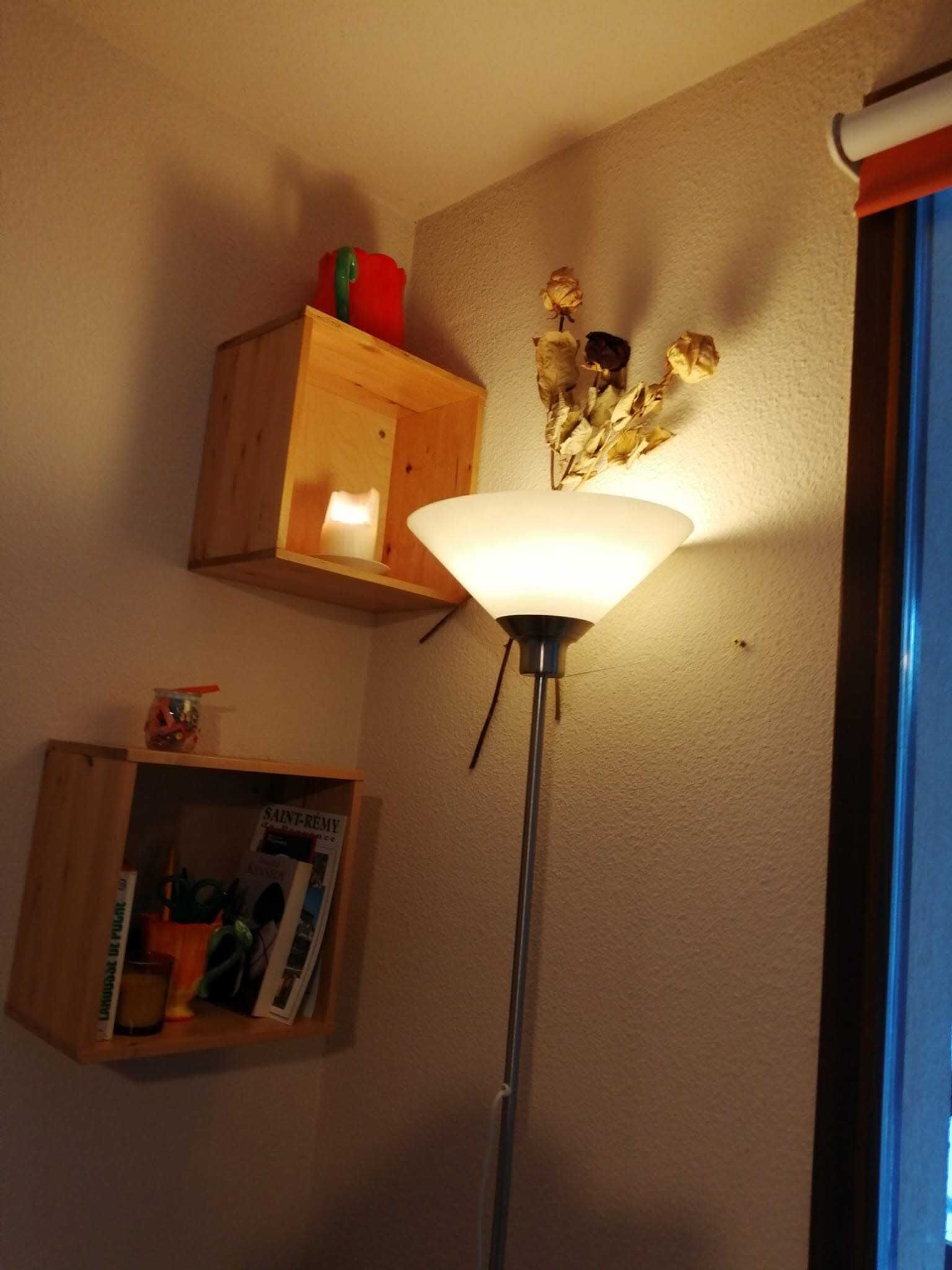 Een kamer met een vloerlamp, een houten plankje met een kaars, en een decoratie aan de muur.