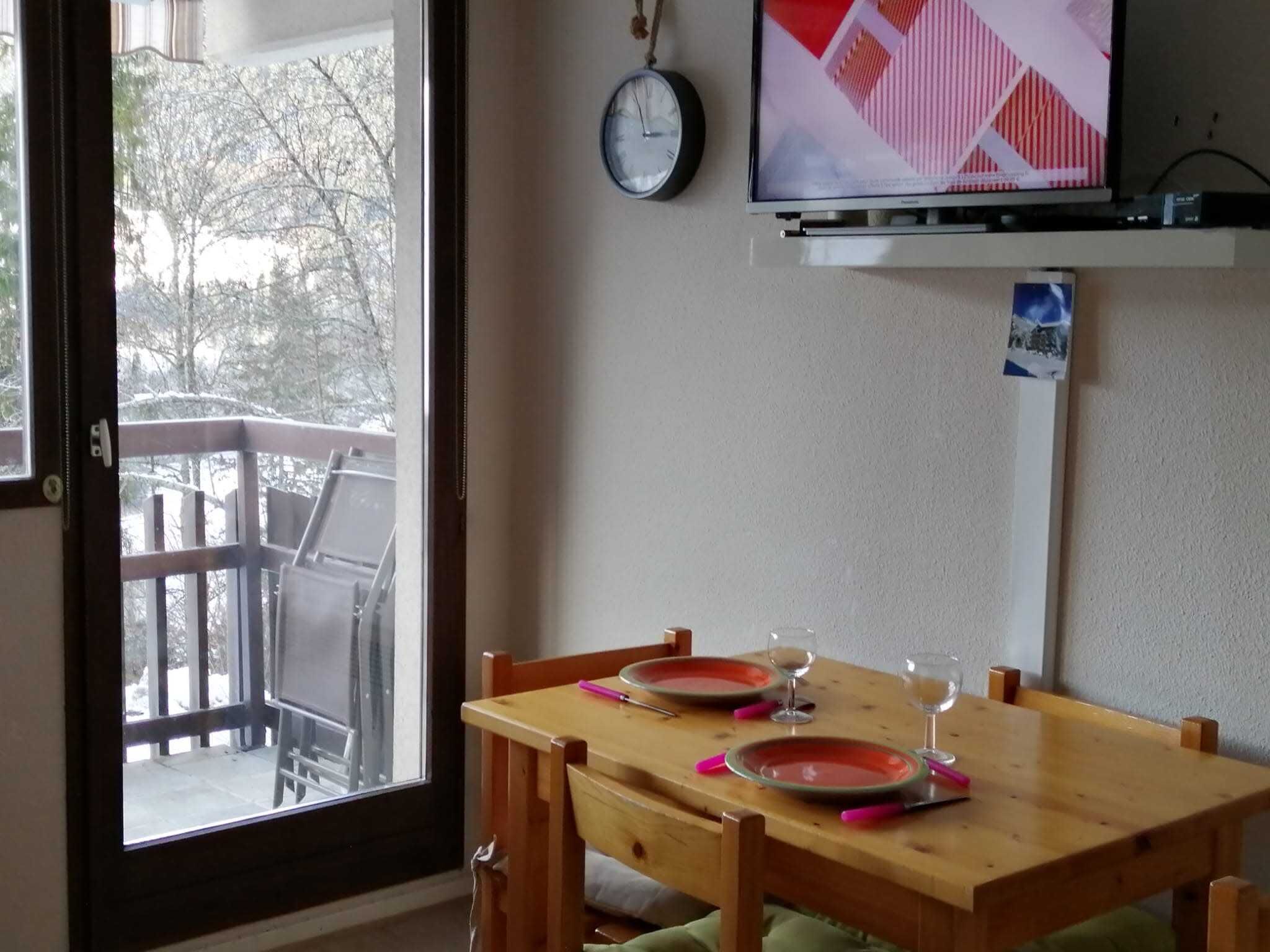 Ein Essbereich mit einem Holztisch, gedeckt für zwei Personen, einer Wanduhr und einem Fernseher, der über dem Tisch angebracht ist.