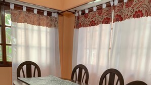 A dining area with a wooden table and chairs, a patterned table runner, and curtains with floral designs.