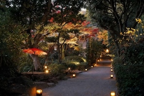 A pathway lined with lanterns and trees, leading to a building entrance. - Tsurumaki Onsen Motoyu Jinya (Hadano)