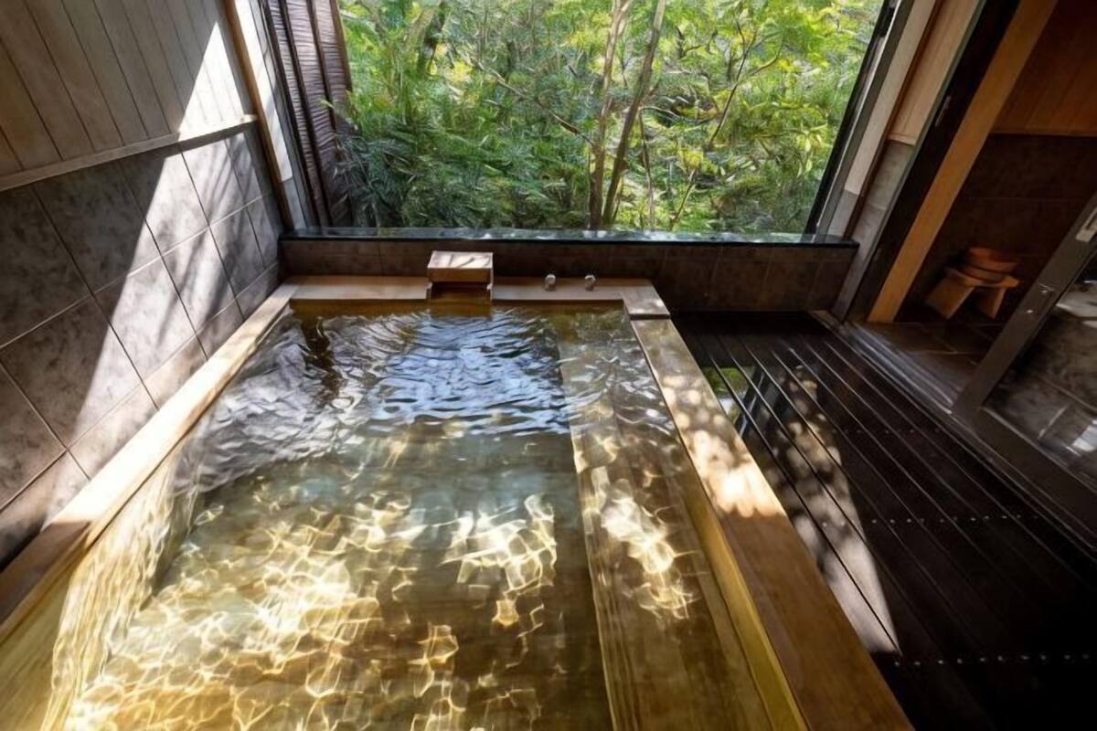 Een hottub met uitzicht op bomen, een houten bankje en een betegelde vloer.