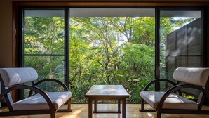 A room with two chairs and a table, large windows with a view of greenery outside. - Tsurumaki Onsen Motoyu Jinya (Hadano)