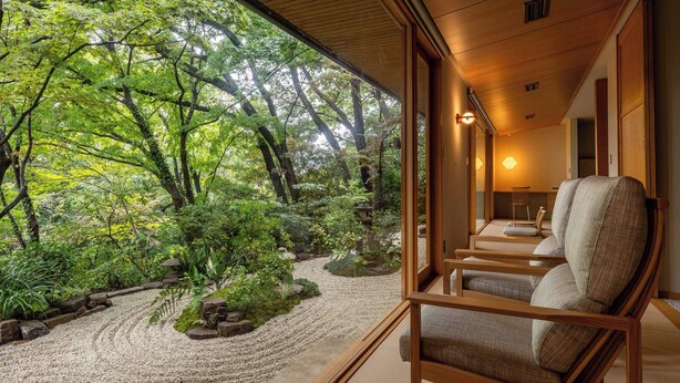 A traditional Japanese-style room with tatami flooring, a low wooden table, and a view of a lush garden with a gravel path and trees. - Tsurumaki Onsen Motoyu Jinya (Hadano)