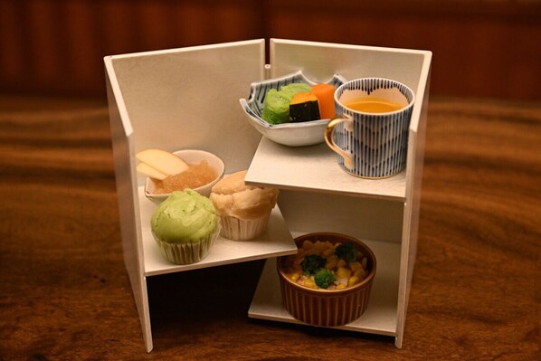 A small, open cabinet with various food items including cupcakes, a bowl of vegetables, and a cup of tea. - Tsurumaki Onsen Motoyu Jinya (Hadano)