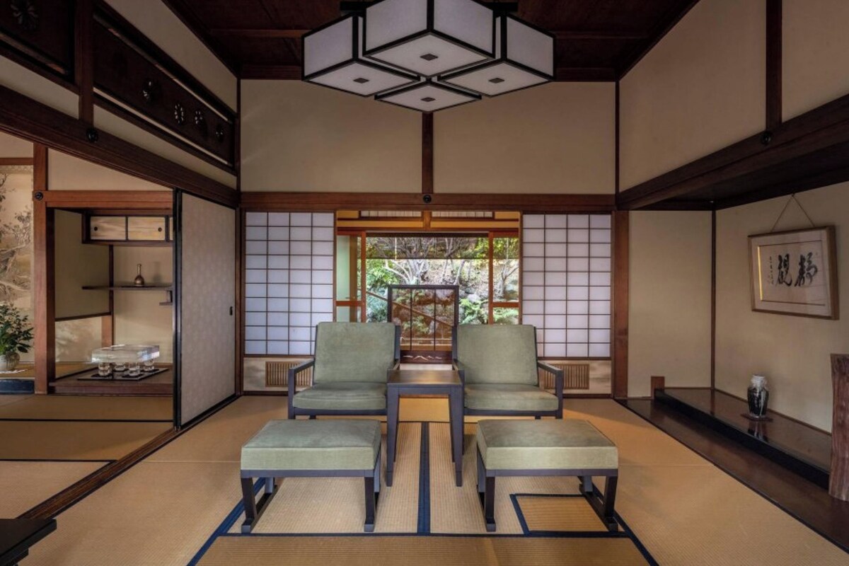 Une pièce de style japonais traditionnel, avec un sol recouvert de tatamis, une table basse, deux chaises vertes et une porte coulissante en papier de riz (shoji).