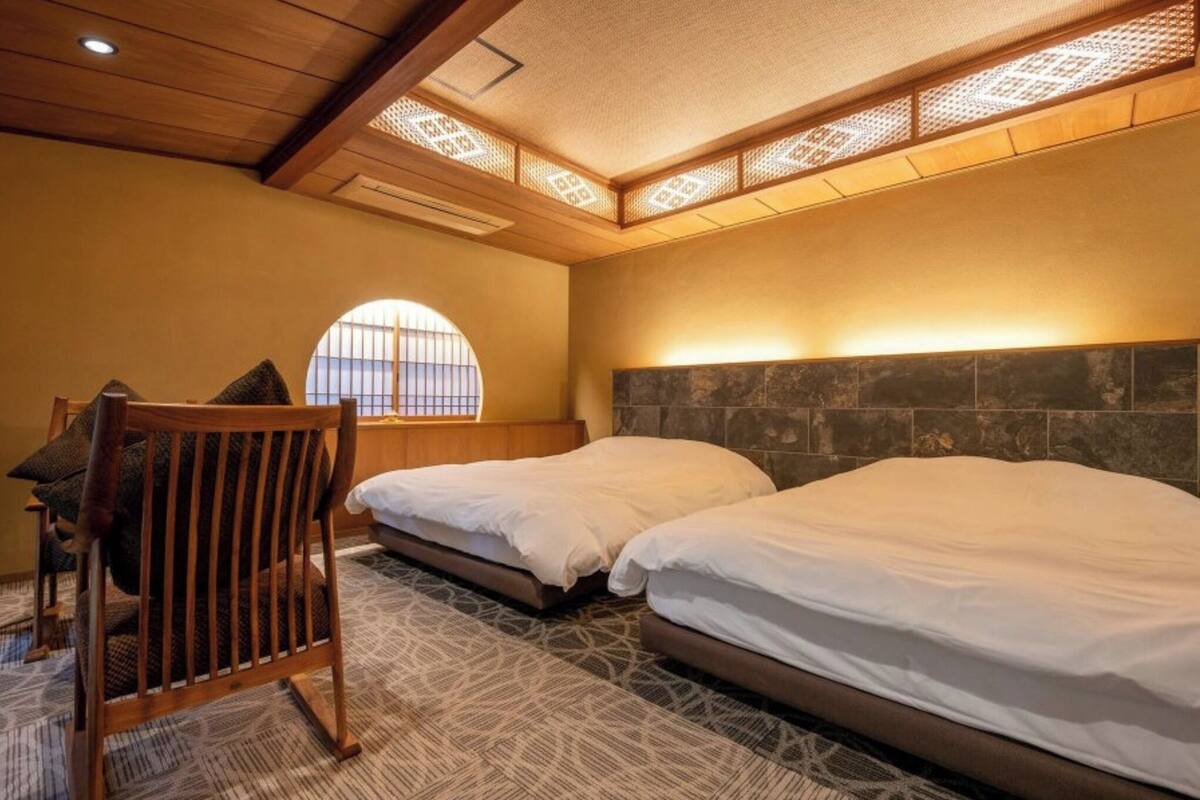 Hotelkamer met twee bedden, een houten stoel, een kamerbreed tapijt met een patroon en een groot raam met uitzicht.