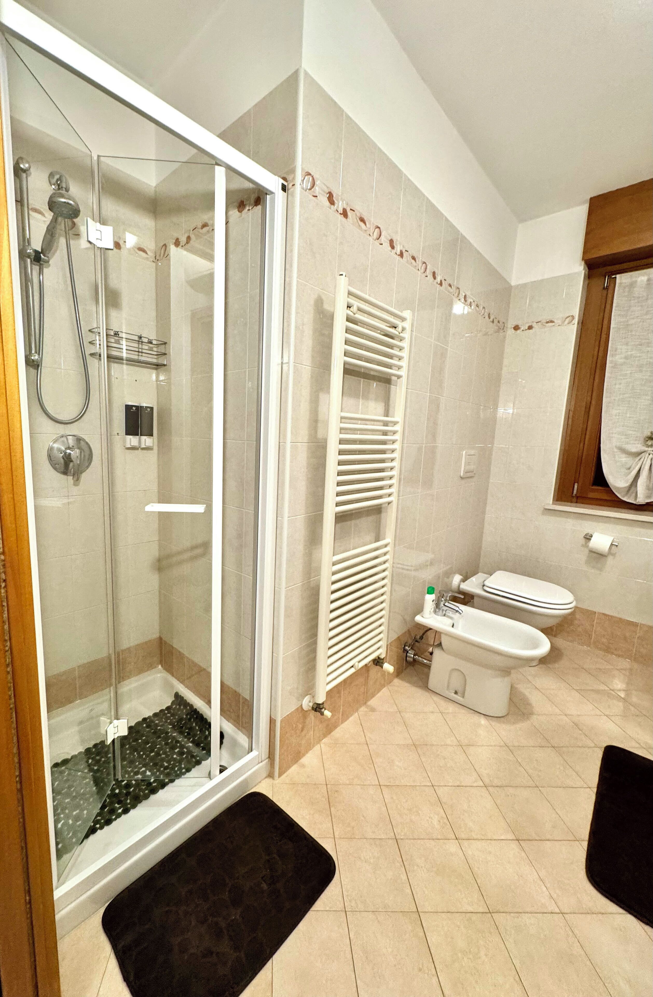 Un bagno con doccia vetro, water bianca e lavabo bianco.