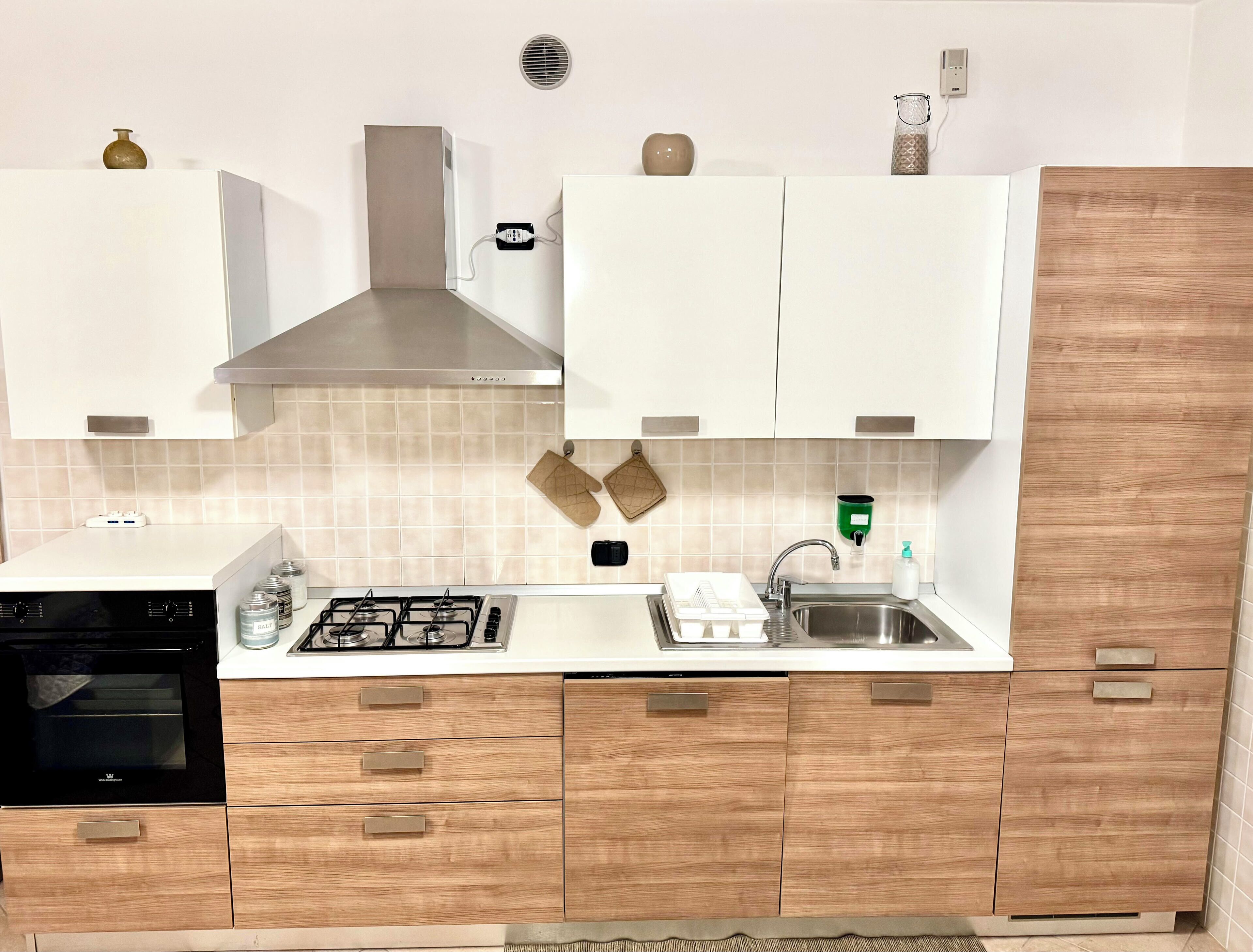 A modern kitchen with white cabinets, a stainless steel sink, a built-in oven, and a gas stove.