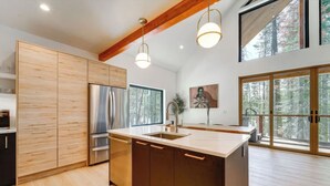 A modern kitchen with wooden cabinets, stainless steel appliances, and large windows offering a view of the forest. - Donner Summit - Hot Tub, Fireplace & Mountain Views (Soda Springs)