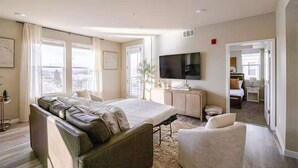 Une chambre d’hôtel moderne dotée d’un grand lit, d’un coin salon, d’une télévision et offrant une vue sur la ville.