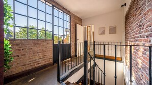 A staircase with a metal railing leading to a second floor, a brick wall, and large windows allowing natural light. - MOT Dorrego 2200 (Buenos Aires)