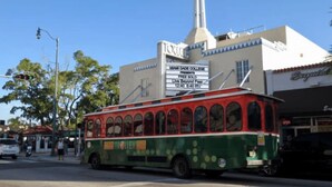 A green and red trolley at a street intersection with a building in the background.