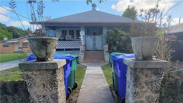 A pathway leading to a house with a fenced front yard, two large planters on either side, and a clear sky.