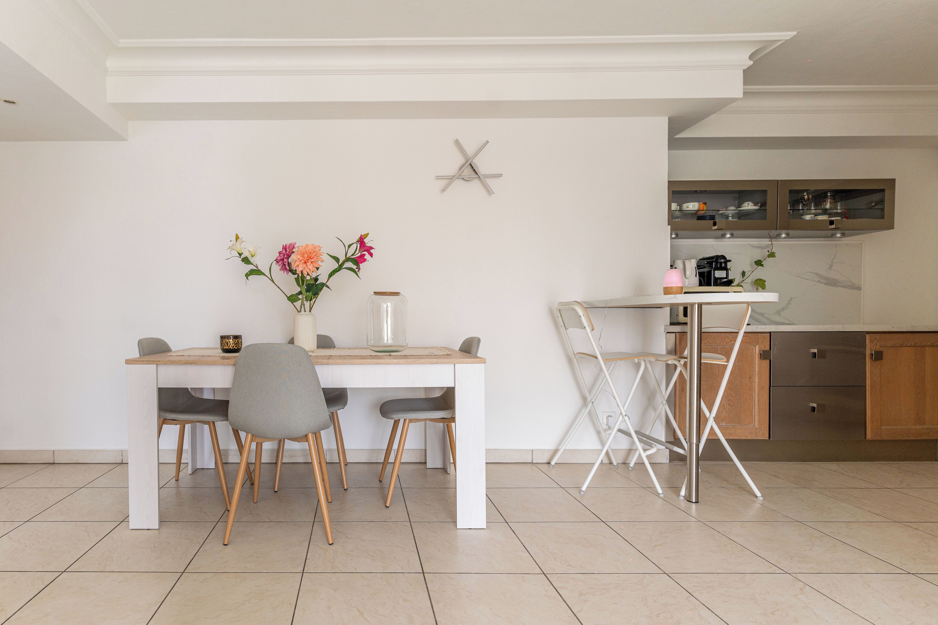 Une cuisine moderne avec des armoires blanches, une hotte de cuisinière en acier inoxydable et un coin repas comprenant une table et des chaises en bois.