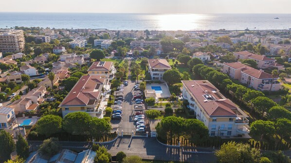 Zona residencial con un edificio grande que tiene piscina, rodeado de vehículos estacionados y vegetación.