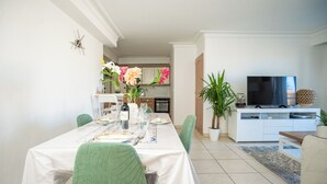 A dining area with a white table set for four, green chairs, and a kitchen in the background. - Proche Thalazur et plages, Parking privé, Piscine (Antibes)