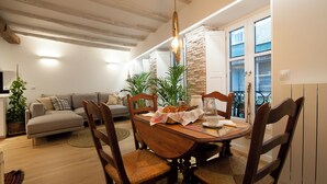 A dining area with a wooden table, chairs, and a chandelier. There is a sofa and a potted plant in the background. - History, comfort, and unique style, just 2 minutes from the beach. (Lekeitio)