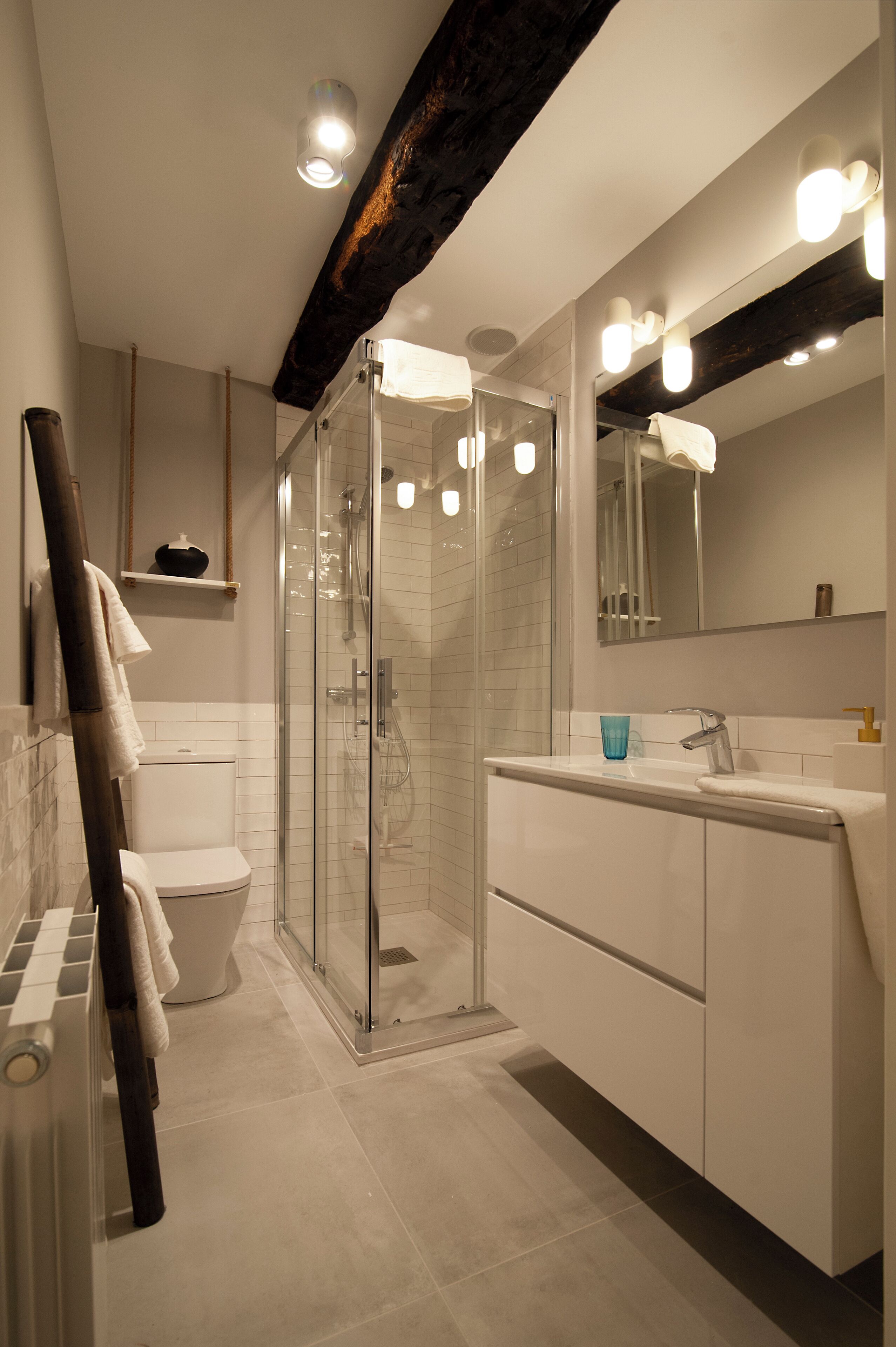 A modern bathroom with a glass-enclosed shower, a white toilet, and a sink with a blue cup.