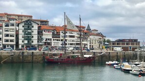 A harbor with a large sailing ship docked, surrounded by buildings with balconies and a white facade. - History, comfort, and unique style, just 2 minutes from the beach. (Lekeitio)
