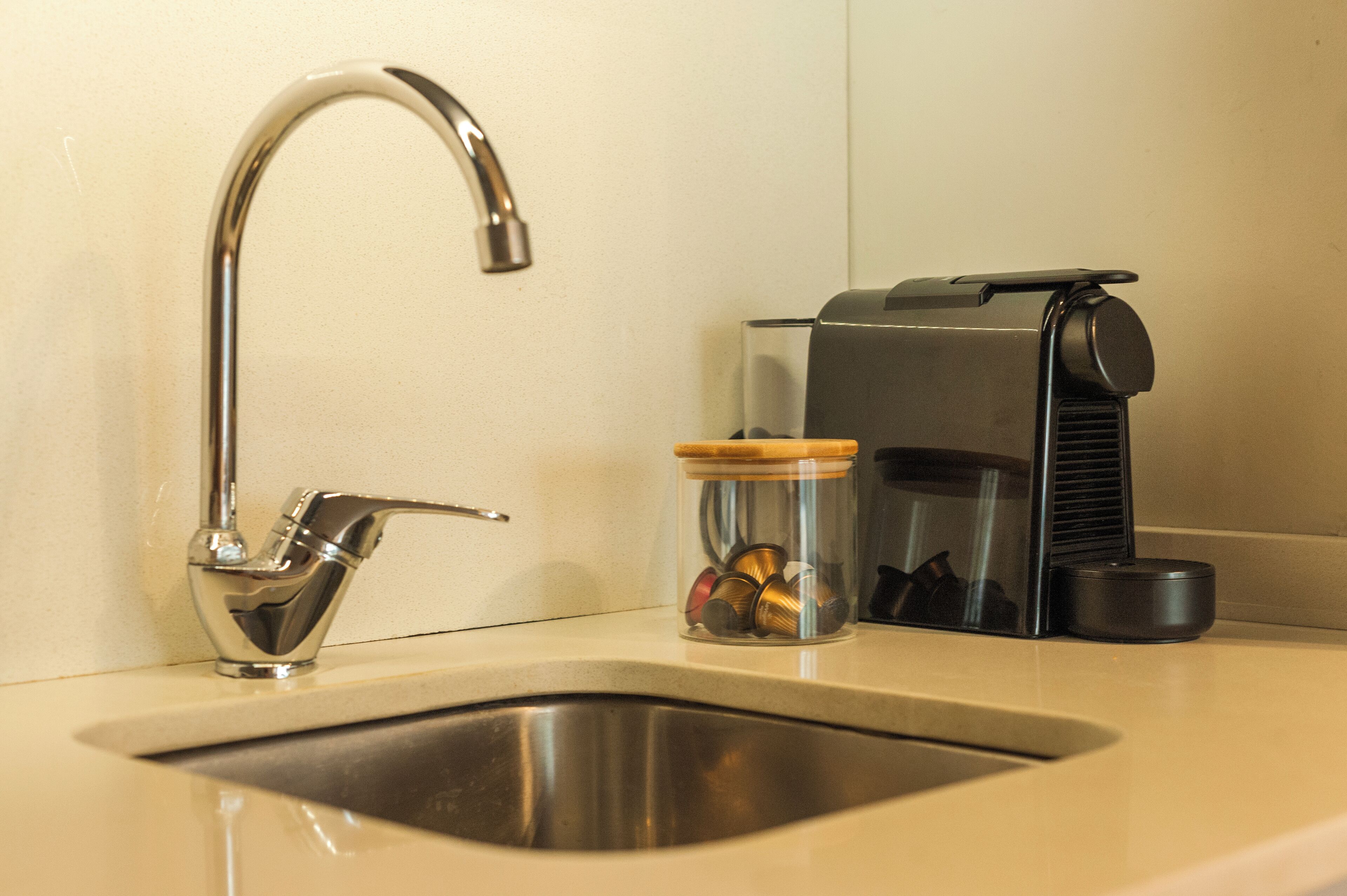 A kitchen sink with a modern faucet, a coffee machine, and a jar of spices.
