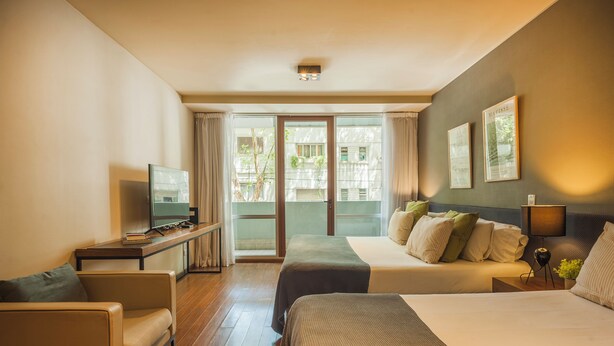 A hotel room with a bed, a sofa, a desk with a TV, and a window with curtains. - Modern High End Studio Palermo T107 (Buenos Aires)