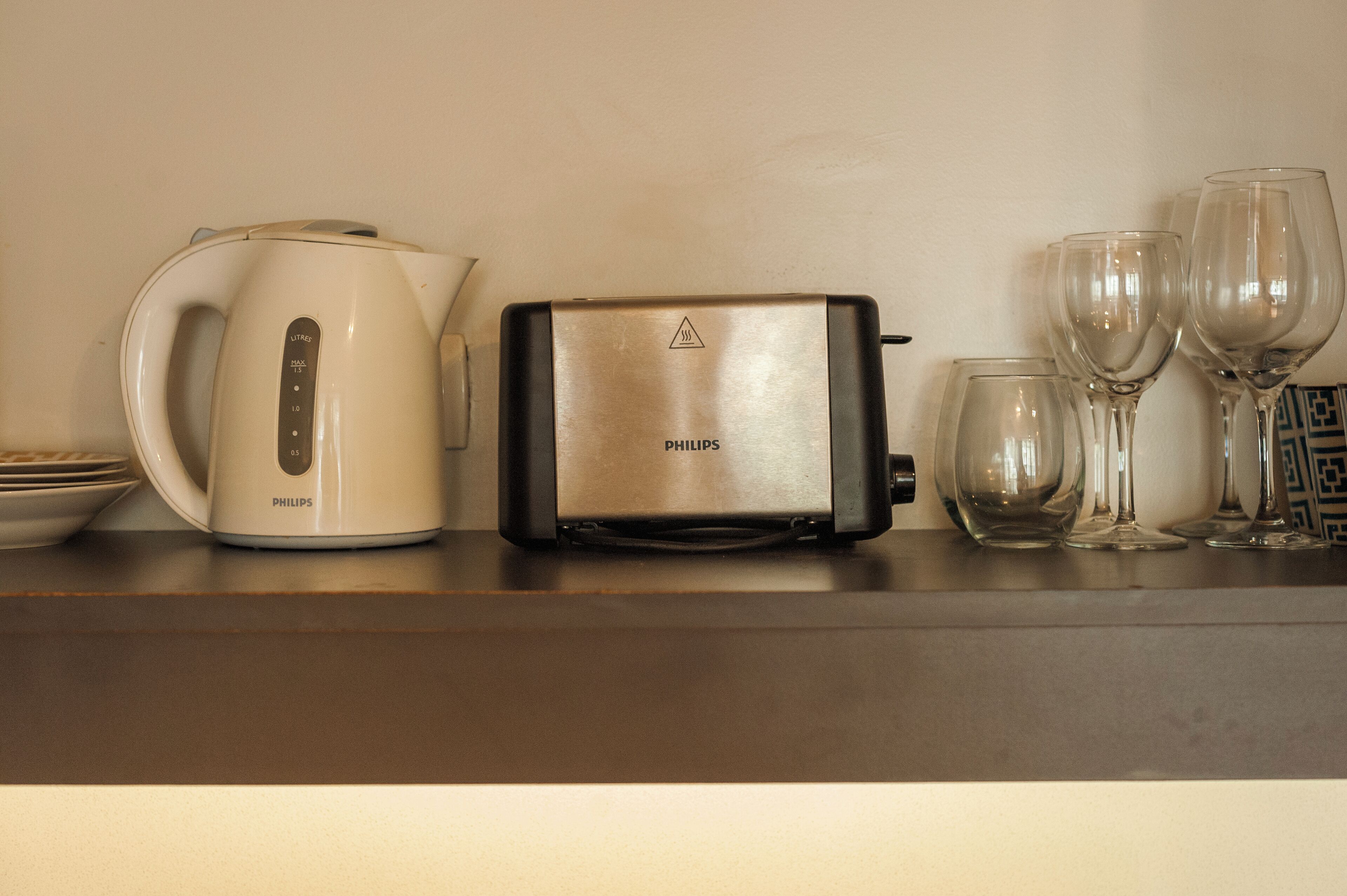 A kitchen counter with a Philips toaster, a white kettle, and several wine glasses.