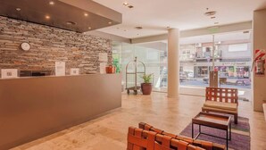 A reception area with a stone wall, a reception desk, a bench, and a view of the street outside. - Modern High End Studio Palermo T107 (Buenos Aires)