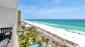 A beach view from a balcony with a pool and umbrellas, a tall building, and a clear sky. - The Summit 1019-toes in the Sand (Panama City Beach)