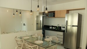Una cocina moderna con un refrigerador de acero inoxidable, un microondas y una mesa de comedor de vidrio con sillas.