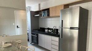 Una cocina moderna con un refrigerador de acero inoxidable, un horno empotrado y un microondas. Hay una mesa de comedor con sillas y una superficie de vidrio.