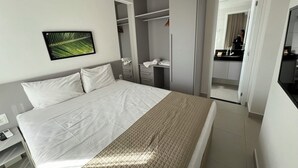 Habitación de hotel moderna con una cama grande, un armario, un baño y un escritorio pequeño con un teléfono.