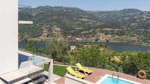 Zona de piscina con dos tumbonas y un flotador, con vistas a un lago y un paisaje montañoso.