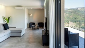 Un moderno salón con un sofá seccional gris, un mueble de TV negro y vistas a un paisaje montañoso a través de un balcón.
