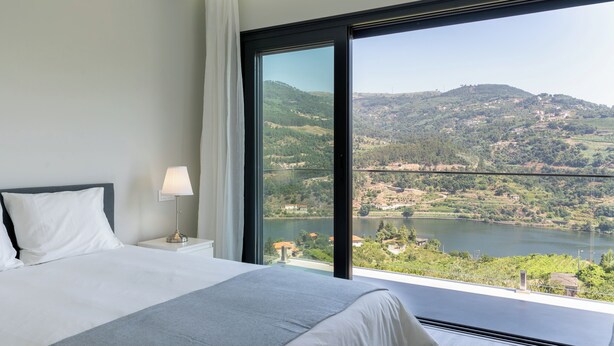 Un dormitorio con un ventanal que ofrece vistas a un lago y colinas.