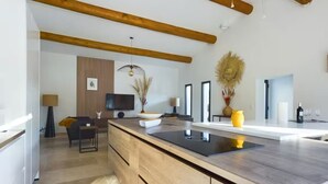 A modern kitchen with a wooden island, a dining area with a sofa, and a TV mounted on the wall. - House at the foot of the Alpilles (Saint-Rémy-de-Provence)