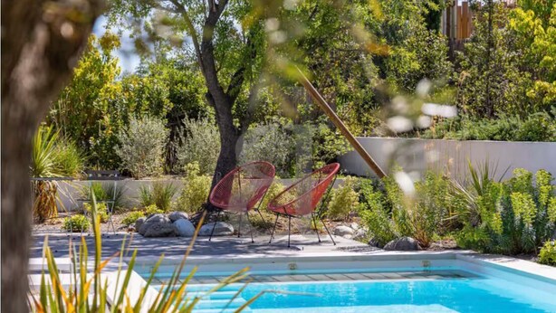 A swimming pool with two red chairs and surrounding greenery. - House at the foot of the Alpilles (Saint-Rémy-de-Provence)